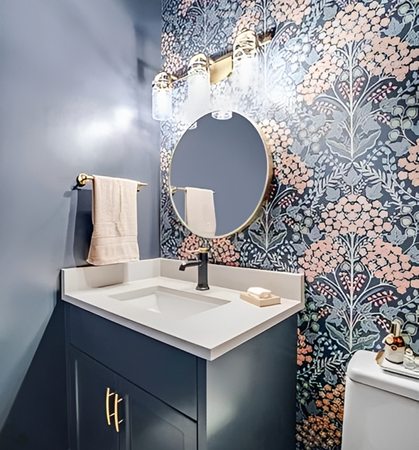 Bathroom with floral wallpaper and round mirror.