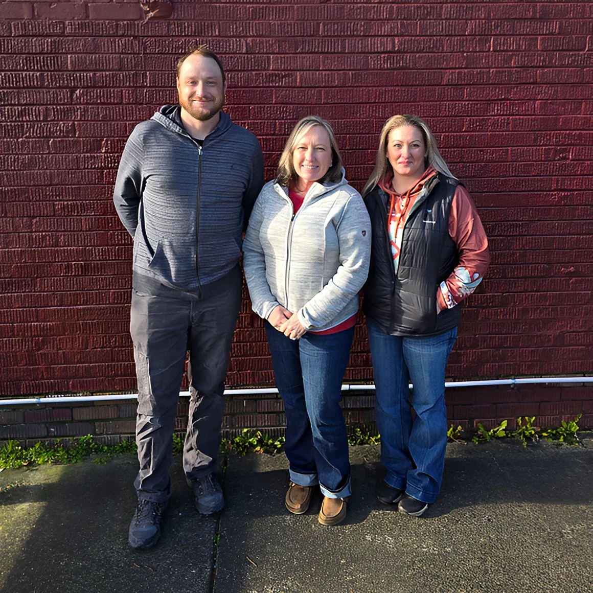 Three people standing against a brick wall.